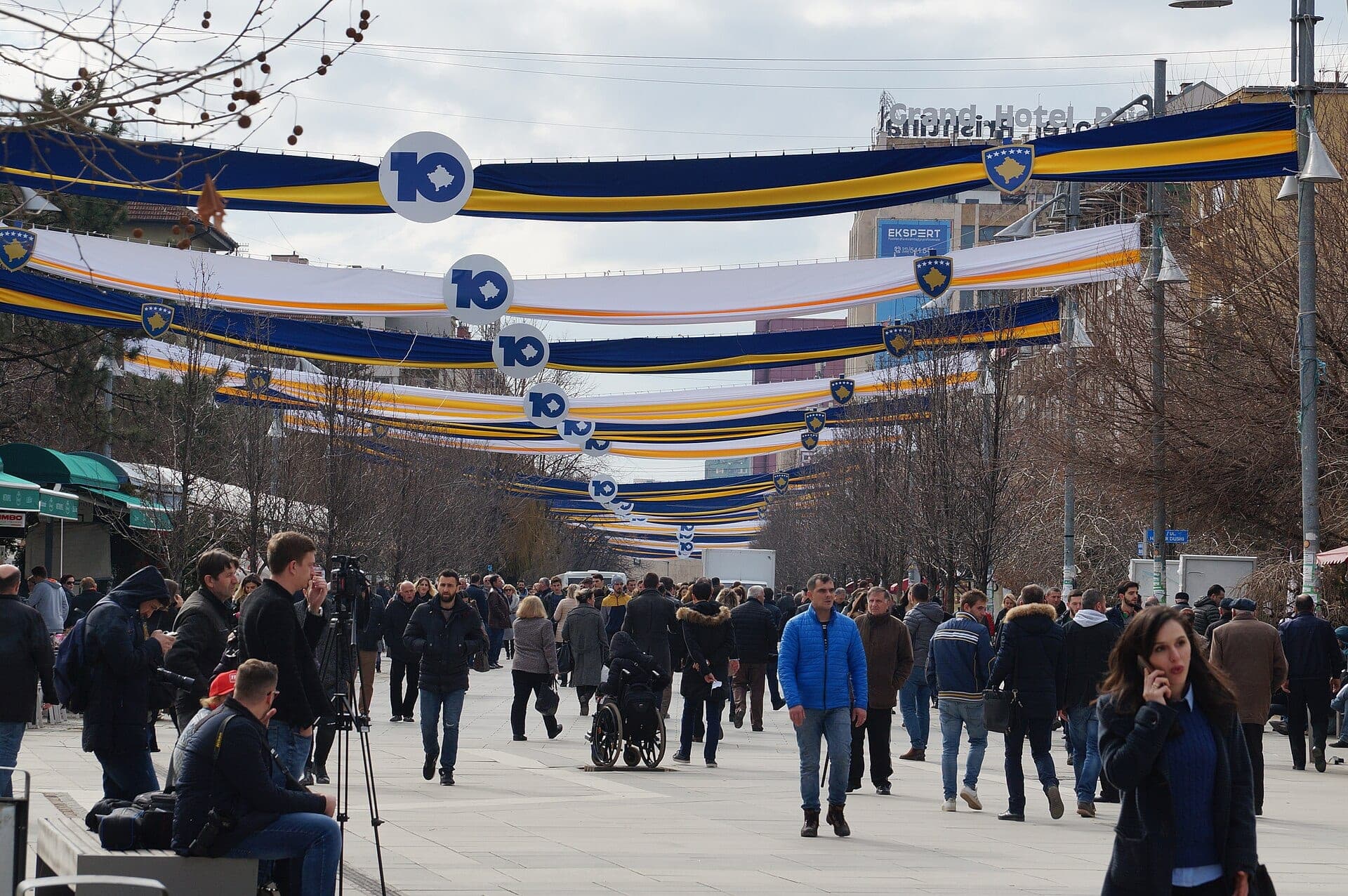 People walking on Mother Teresa Boulevard in Prishtina, with press cameras in the foreground